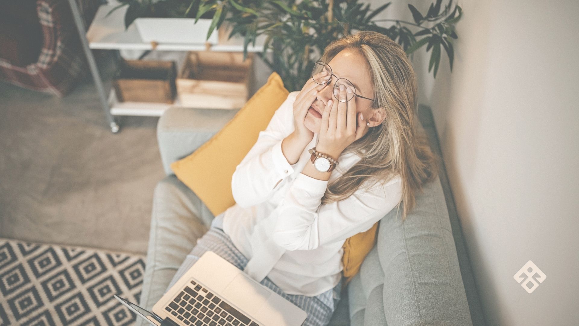 Woman on sofa rubbing her eyes while working on laptop—illustrating fatigue and the question, why am I tired all the time?